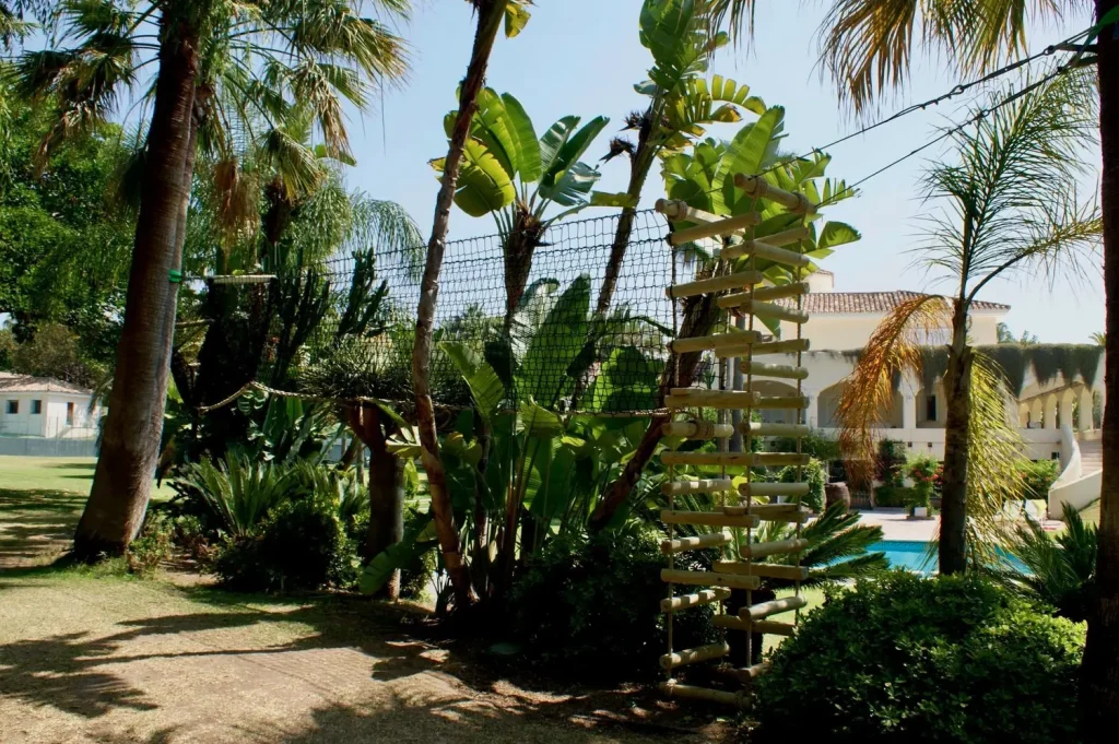 Netted walkway Treetop Canopy Walkway set within Mediterranean palm trees in a family villa garden near a swimming pool.