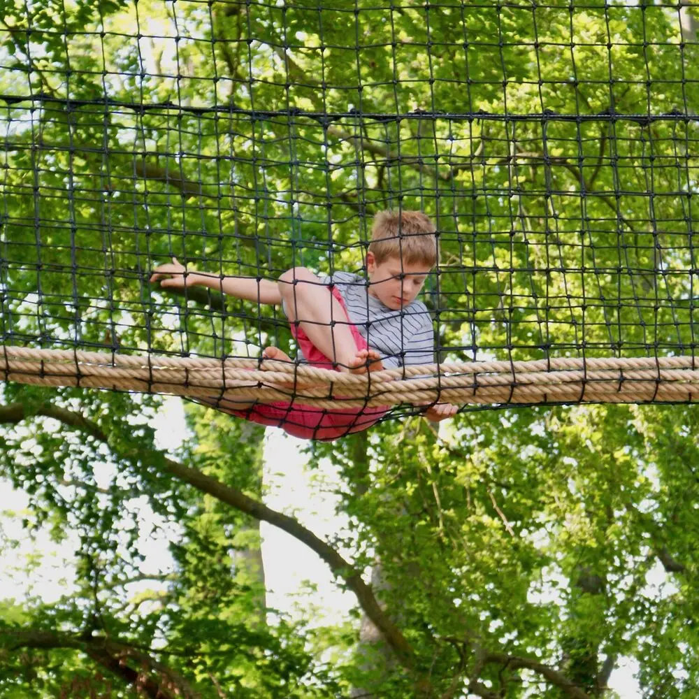 Boy sitting on rope in a netted Treetop Walkway.
