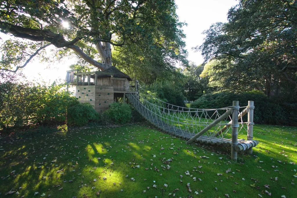 Garden Treehouse set into lawn and trees with large Log Rope Bridge entrance.