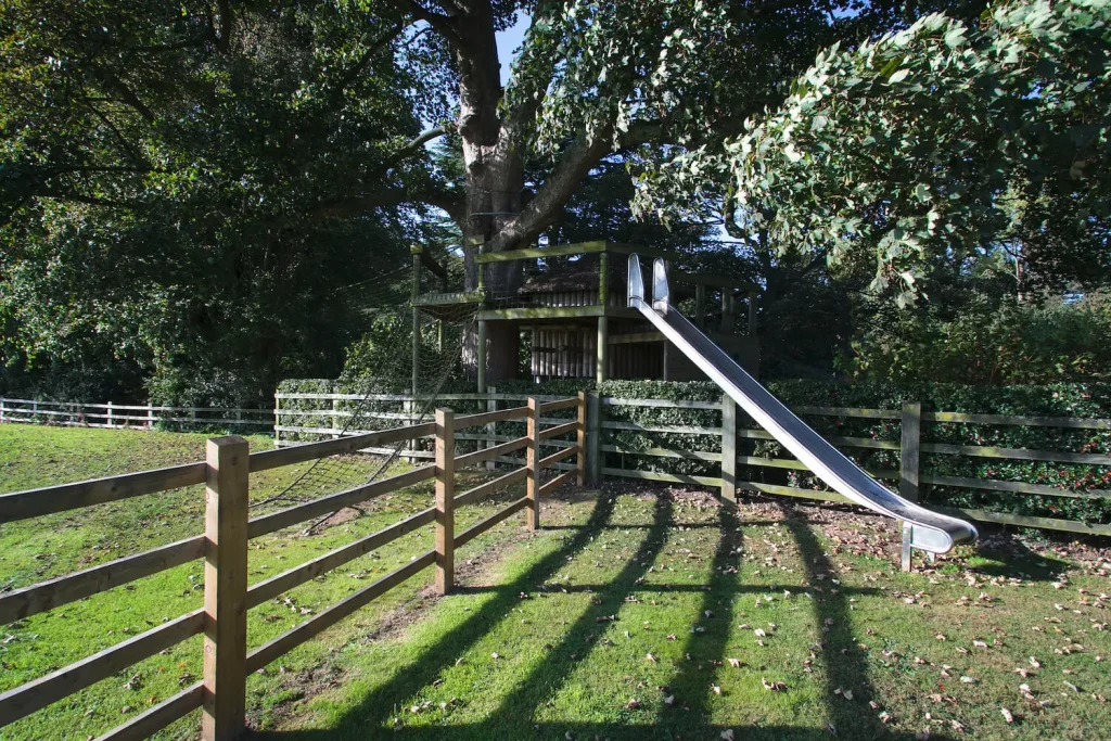 Treehouse set around tree with a large Slide leading into an open garden field.