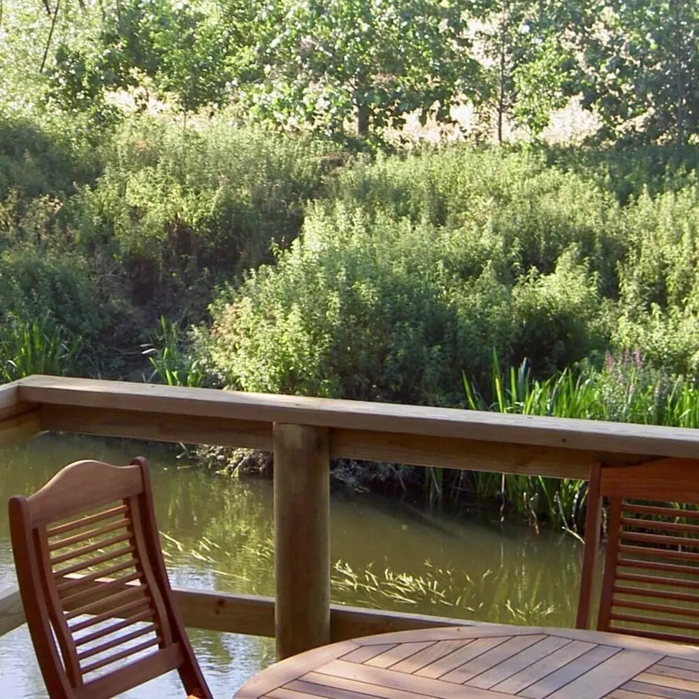 Table and chairs on a deck platform overlooking a river in countryside view.