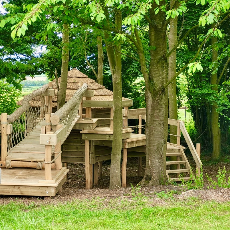 Step Deck and Rope Bridge leading to a thatched roof and timber Treehouse and multi-level Play Deck Platforms with stair steps to the woodland floor