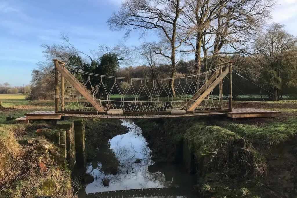 Rope Bridge over a river crossing in field surrounded by trees