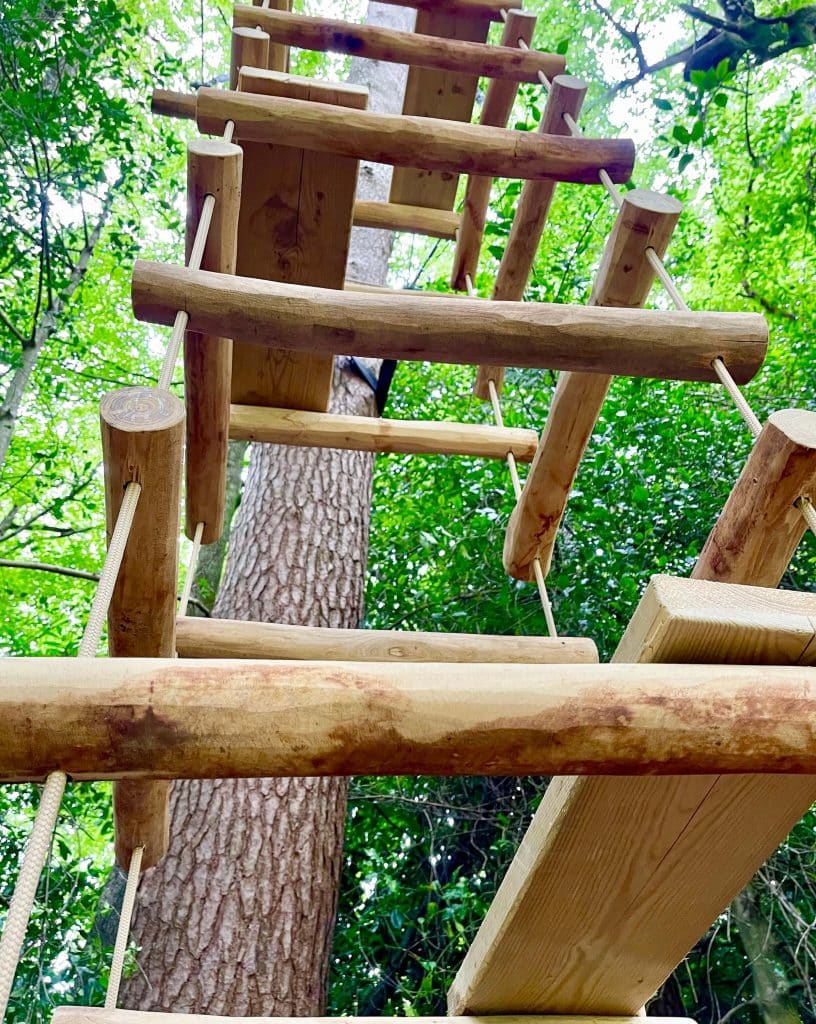 Log Rope Ladder with rungs on 4 sides joined to suspended hemp coloured rope.