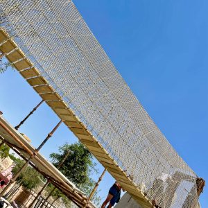 Rope Bridge in Qatar in blue sky, wrapped in beige-hemp coloured safety netting with installation scaffolding underneath for install team to work.
