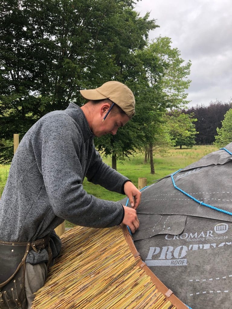 A man thatching a treehouse roof in Surrey, UK.