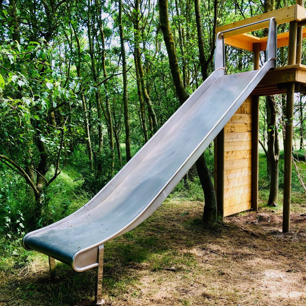A stainless steel double width slide with a climbing wall and suspended tree deck.